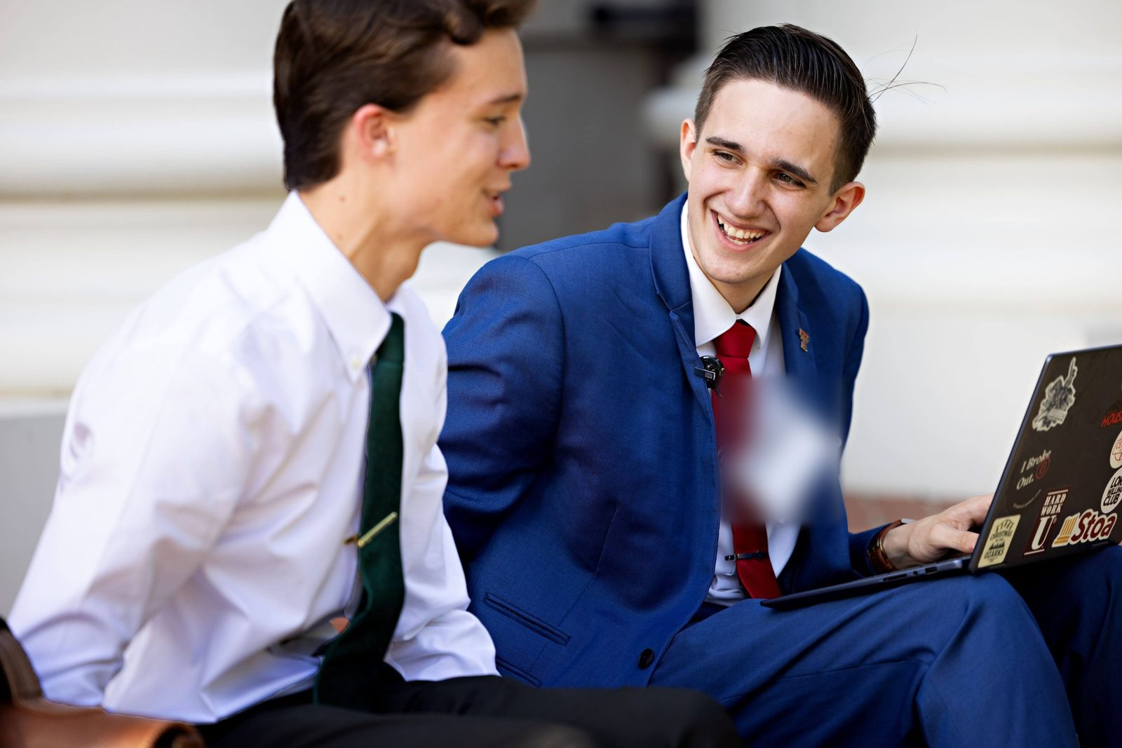 Two debaters laughing over a laptop on the steps